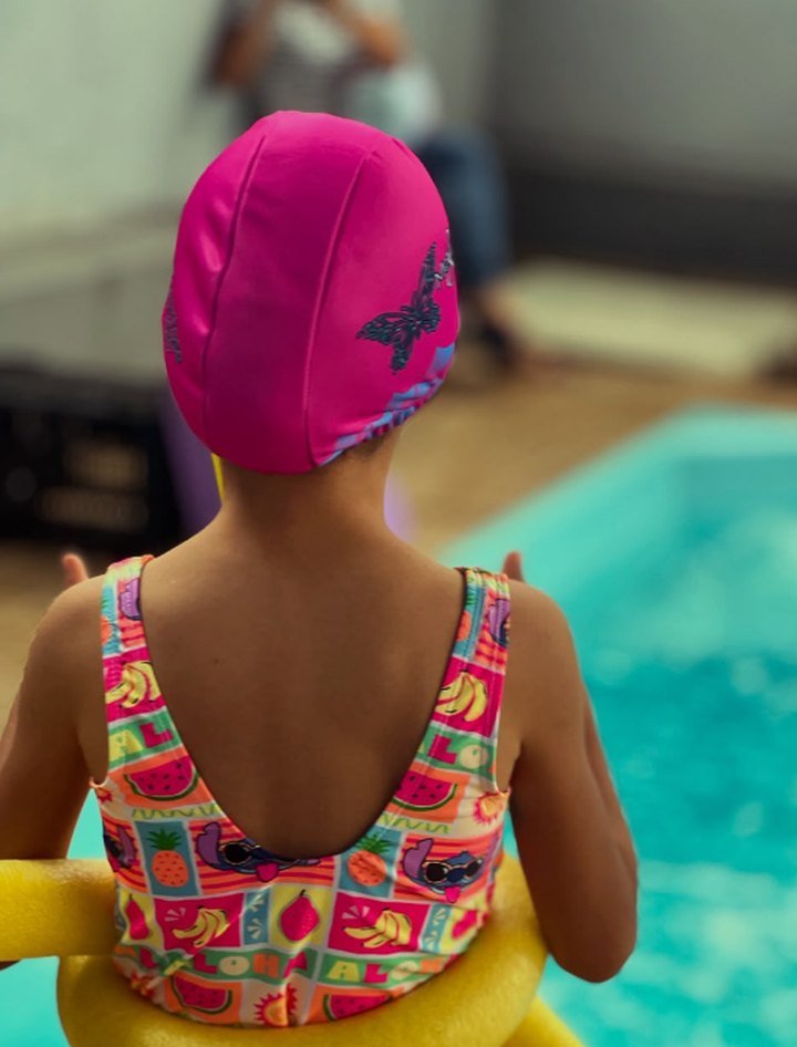 Criança com touca de borboleta à beira da piscina, pronta para a natação infantil
